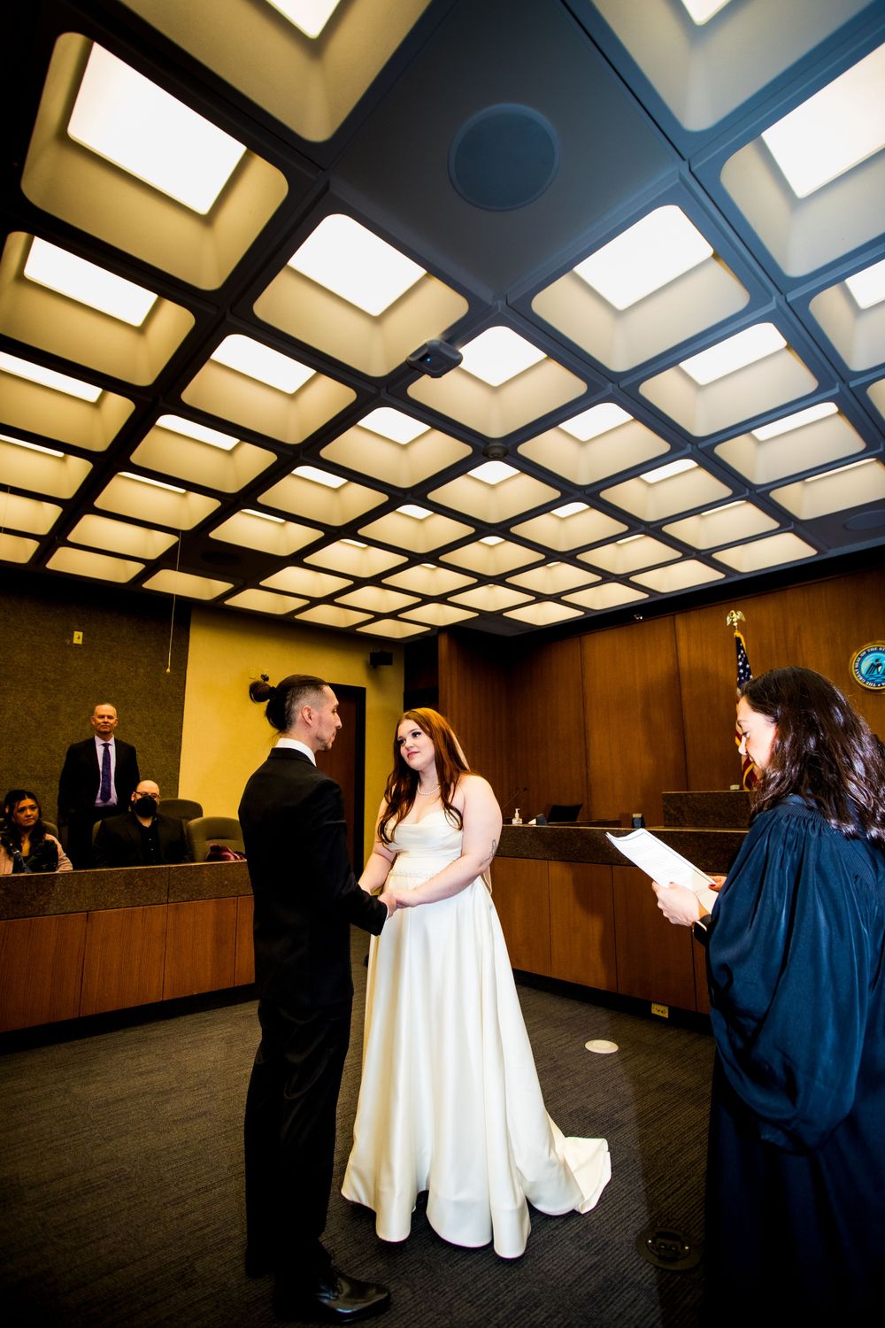Wedding ceremony under geometric ceiling lights in an official building room.