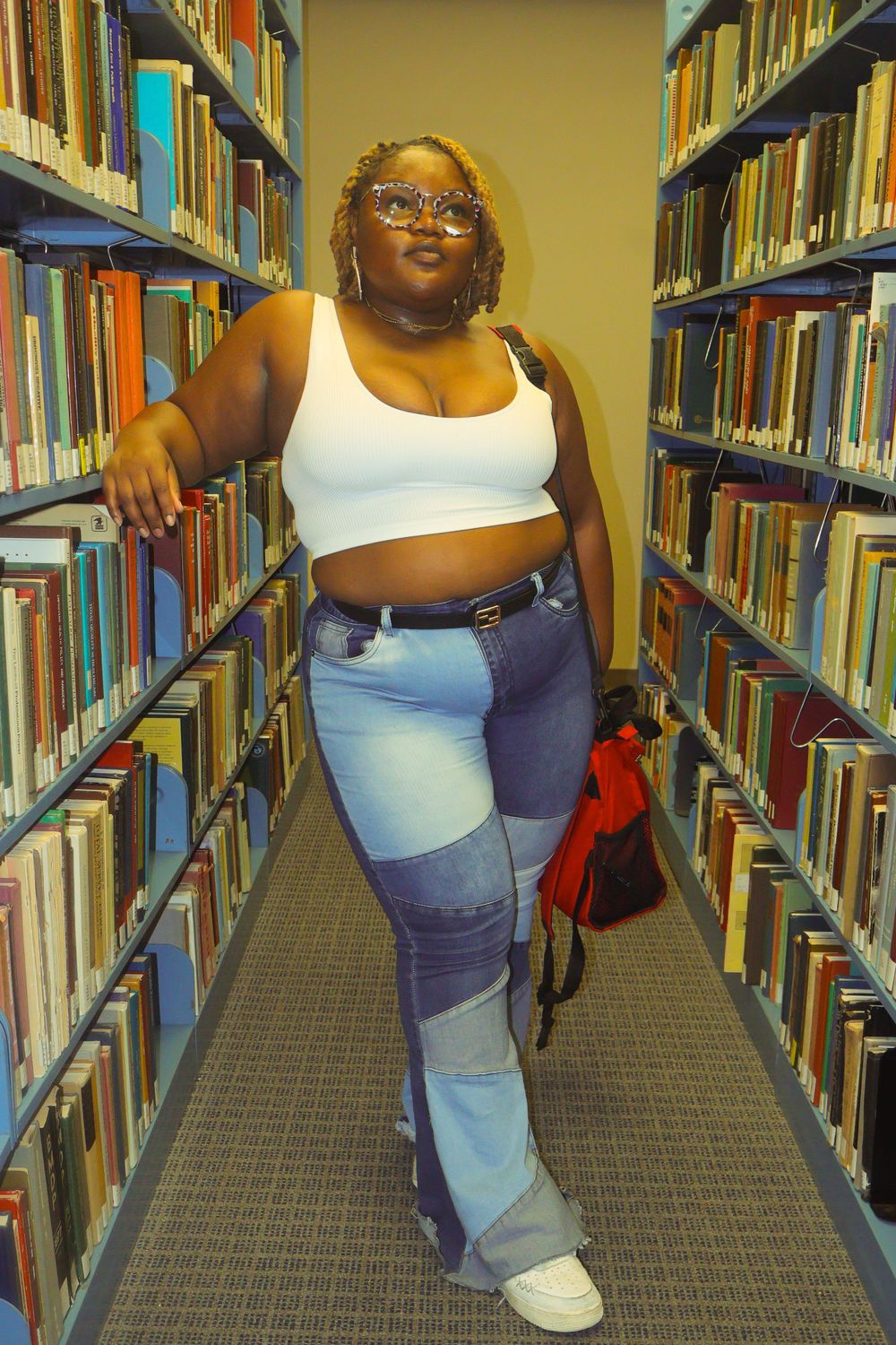 Person browsing books in library stacks wearing casual attire.