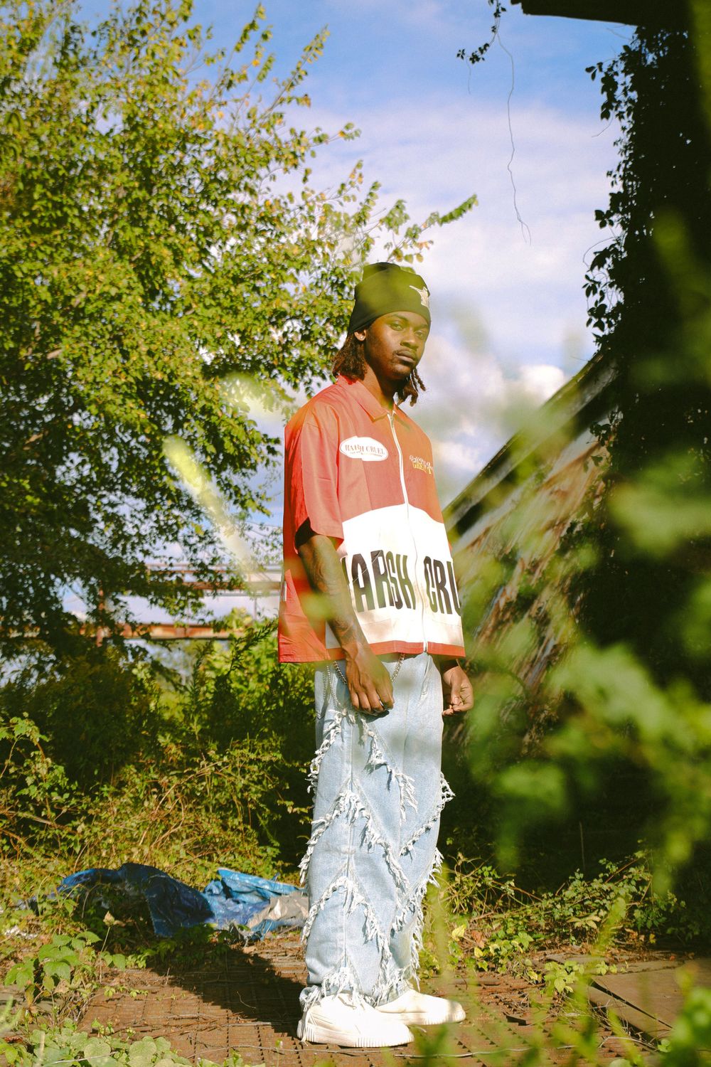 Figure standing outdoors wearing red and white clothing among green foliage.