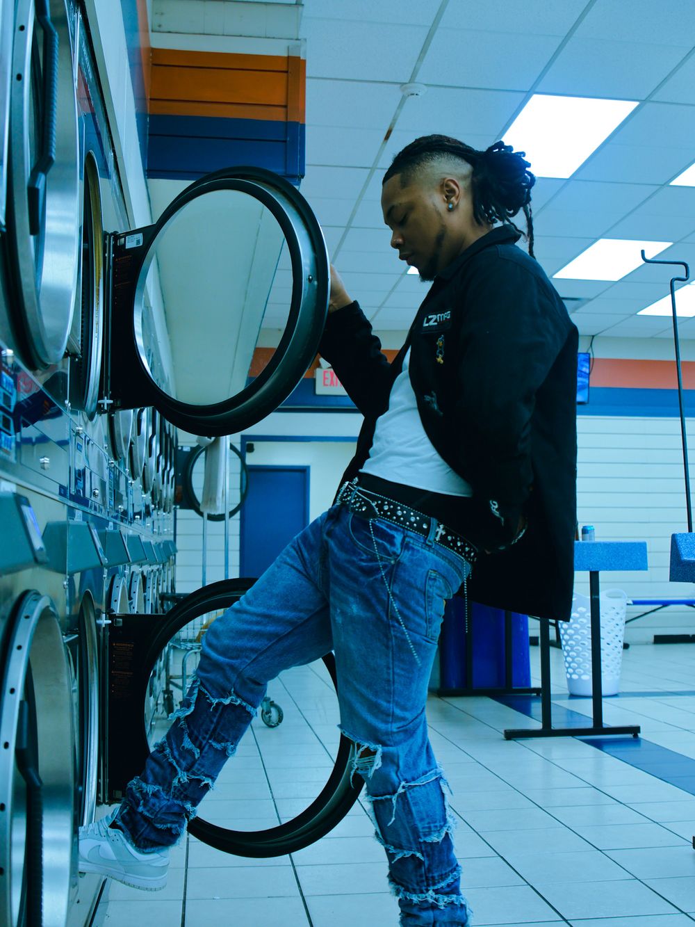 Person in denim clothing looking through a laundromat's washing machines.