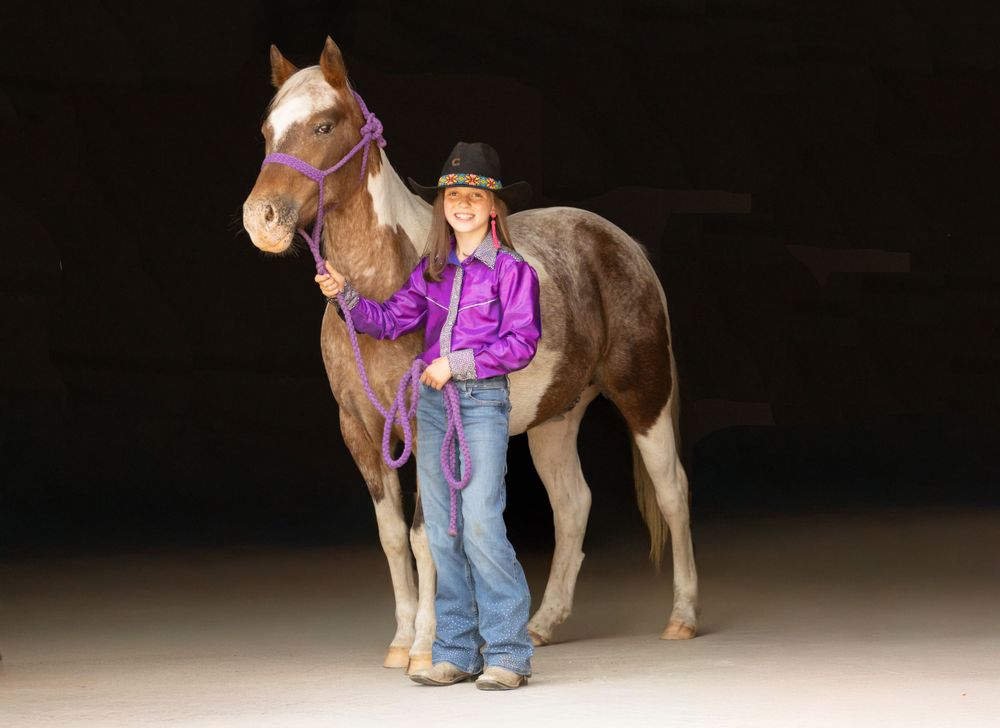 Horse and rider in western attire pose against black backdrop with purple accents.