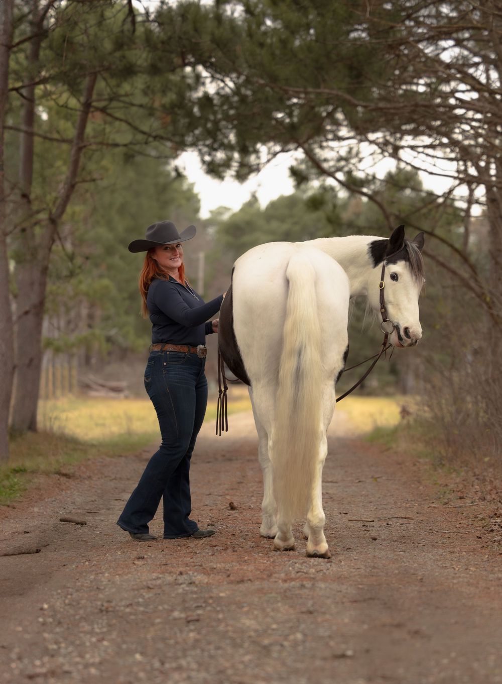 Person leading a majestic white horse down a forest trail on a sunny afternoon.