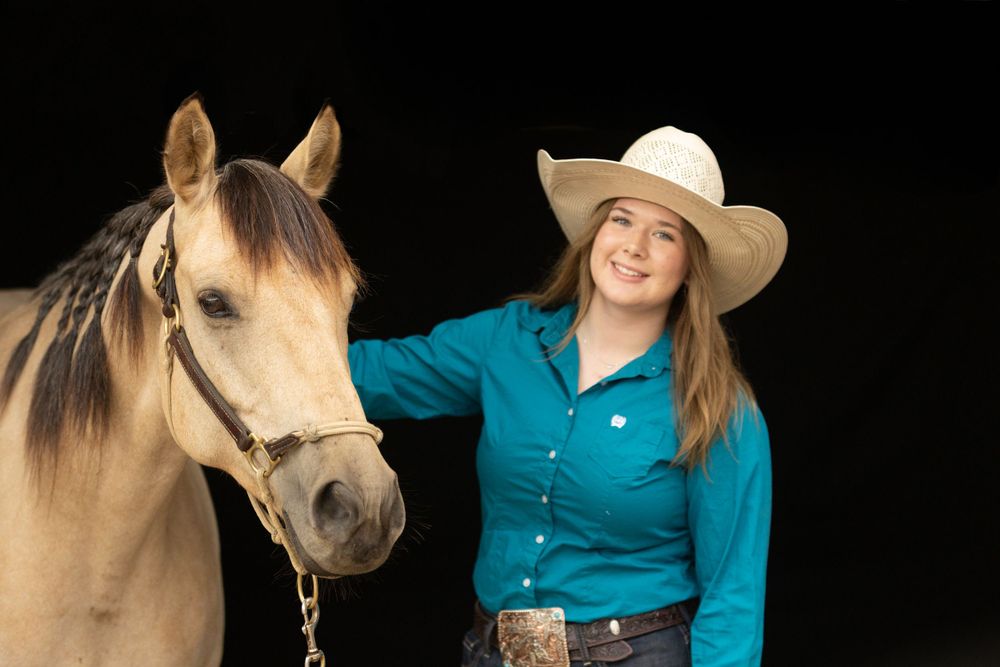 Western style portrait with buckskin horse against black background.