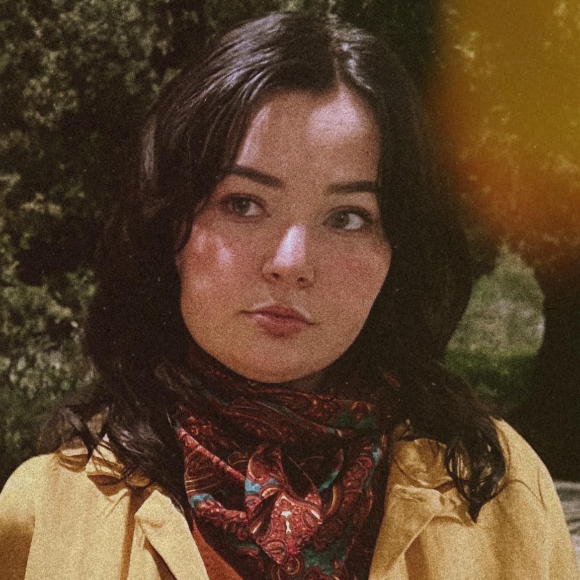 Vintage-style portrait of a woman wearing a yellow jacket and red patterned bandana against a blurred natural background.