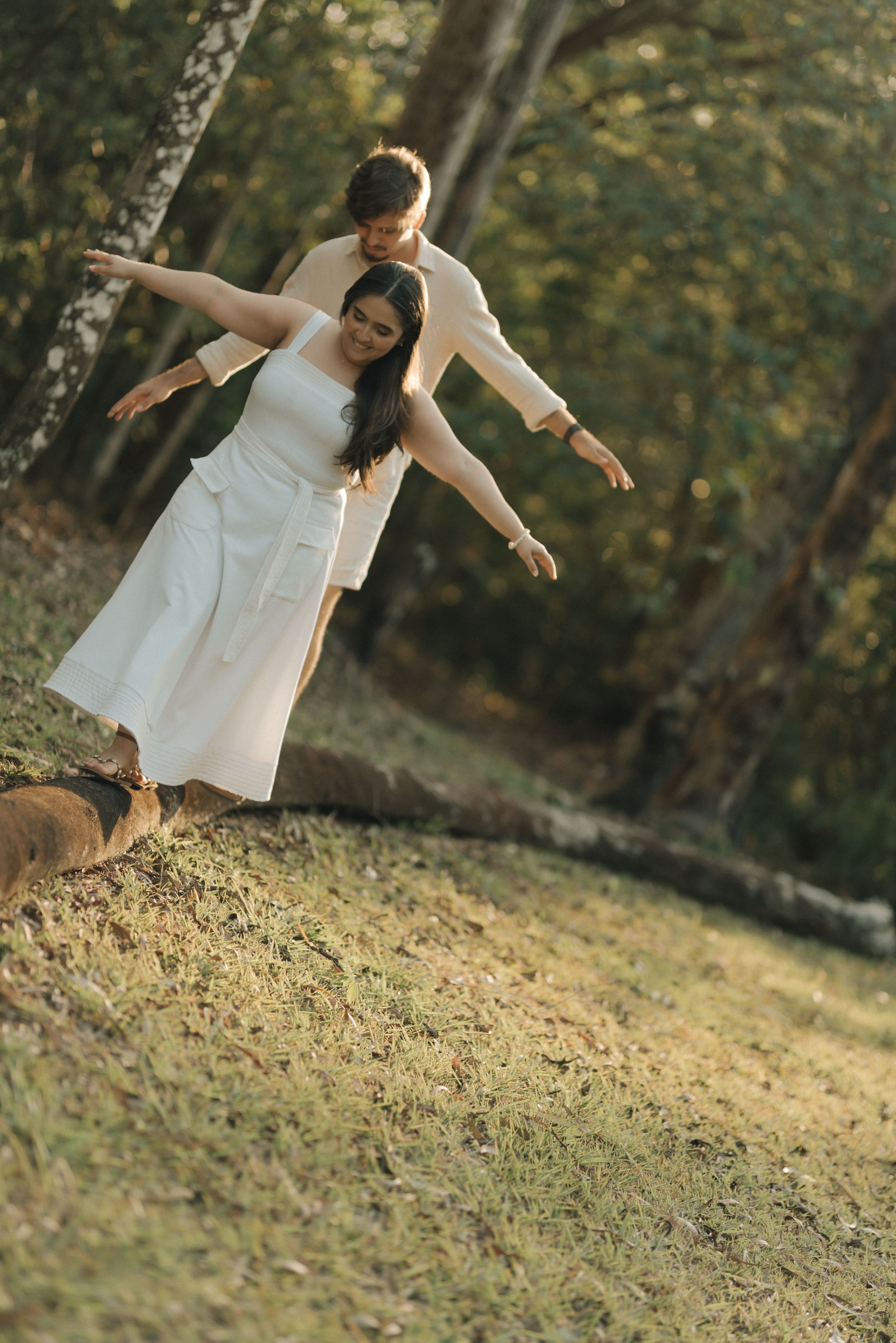 Two people playfully balance with outstretched arms in a natural outdoor setting.