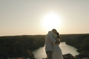 Silhouetted couple embracing against scenic lake view at sunset.