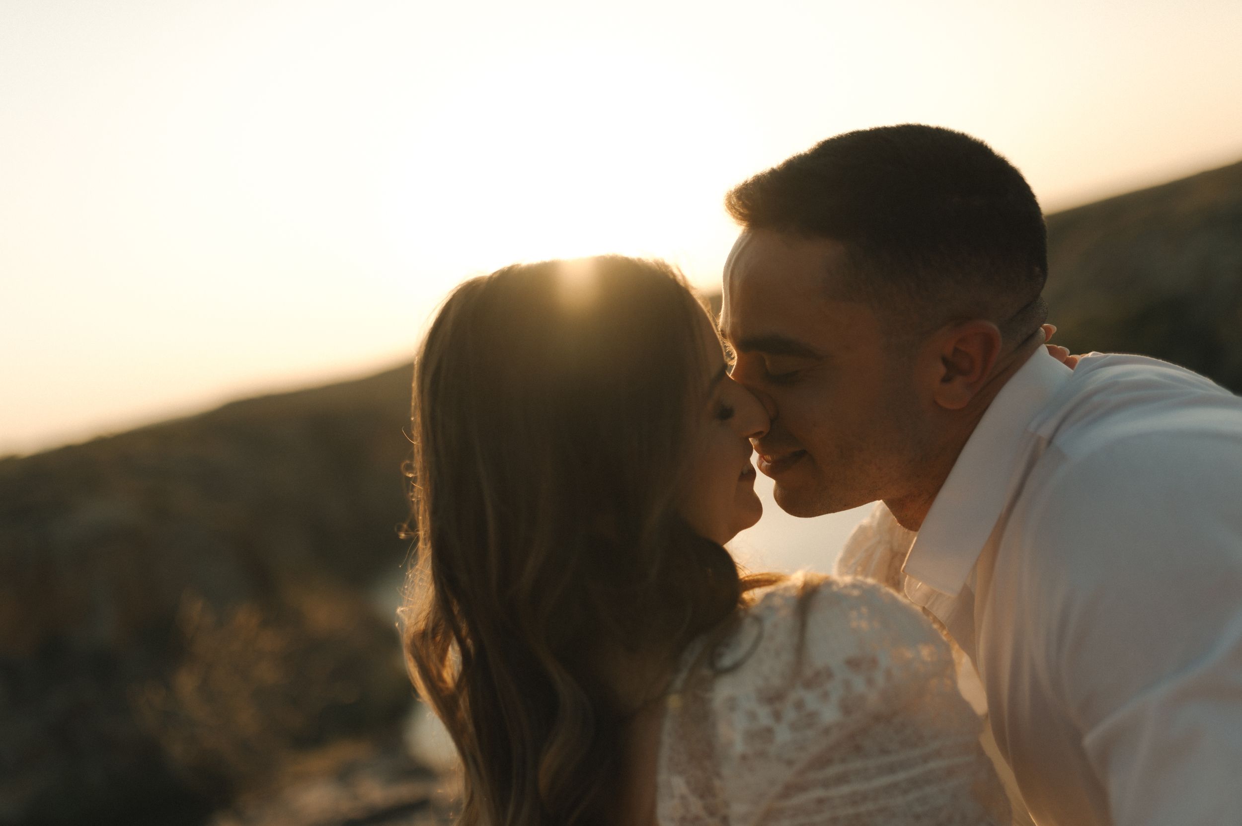 Romantic silhouette of couple sharing an intimate moment at sunset with golden light glowing behind them.