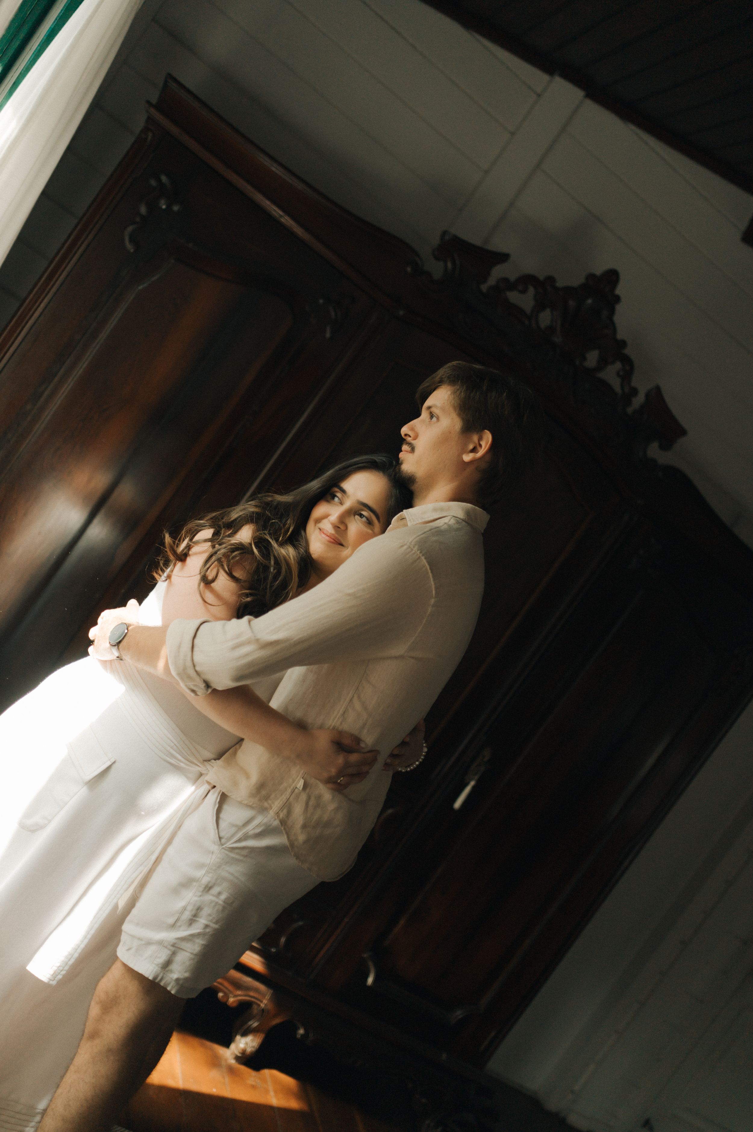 Intimate indoor portrait of a couple embracing in white clothing against a dark wooden door.