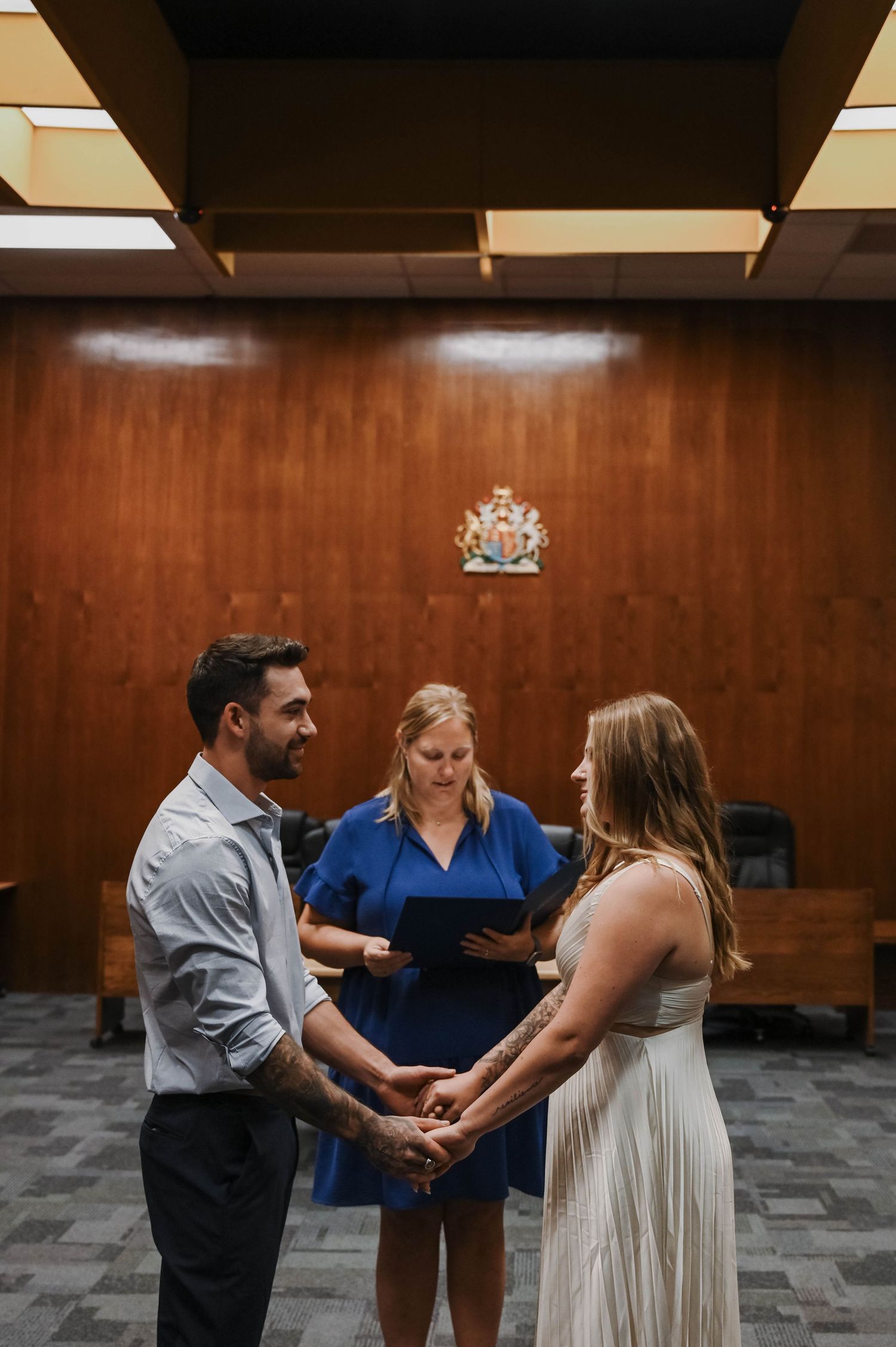 A couple exchanges vows during an intimate courthouse ceremony with an officiant in a blue dress presiding.