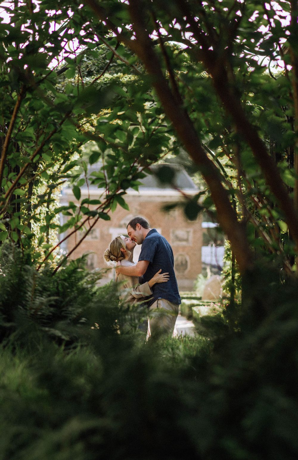 Silhouetted couple embracing through tree branches near a waterfront.
