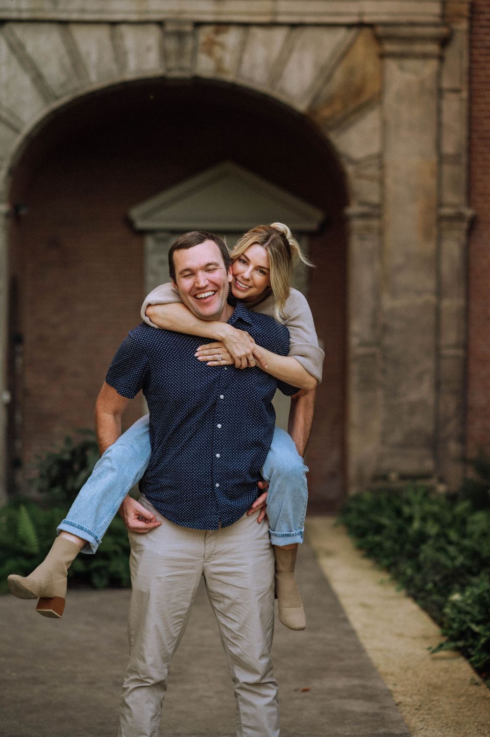 Playful piggyback ride moment between couple in front of stone archways.
