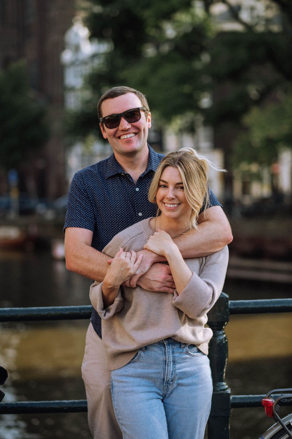 Couple sharing a playful moment along a canal railing during a sunny afternoon.