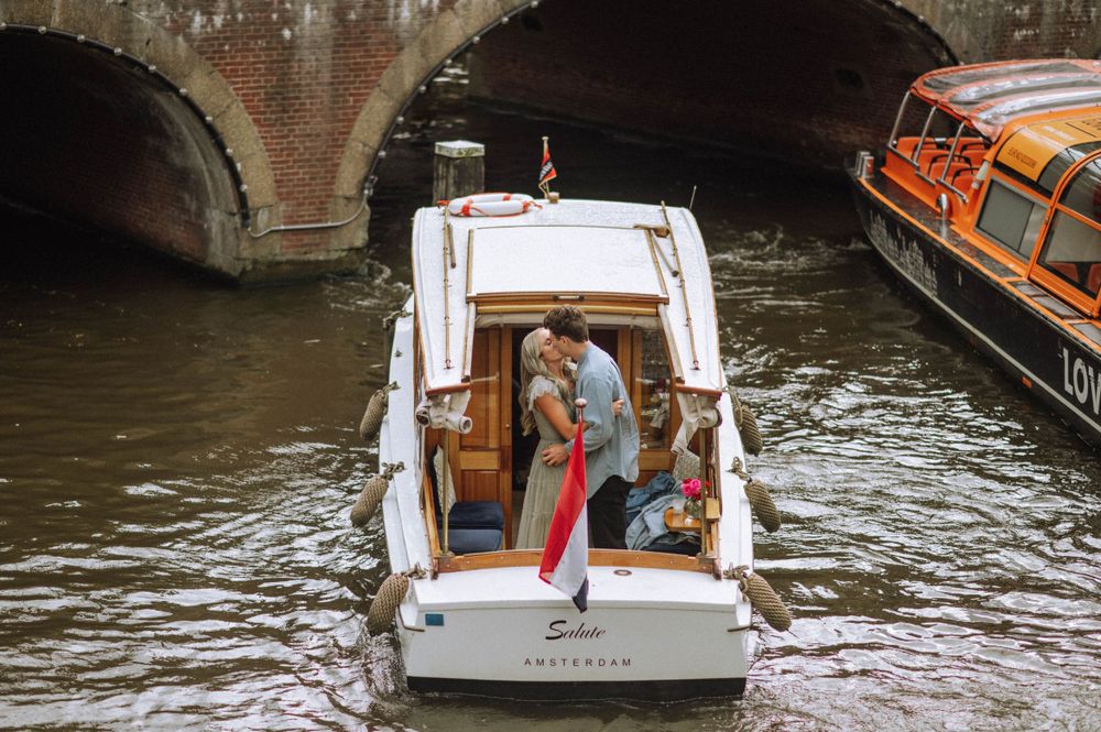 Tourists ride in a white canal boat passing under bridges in Amsterdam.