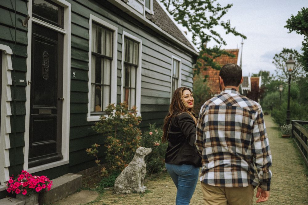 Couple walking past traditional Dutch house with cat watching from doorstep.