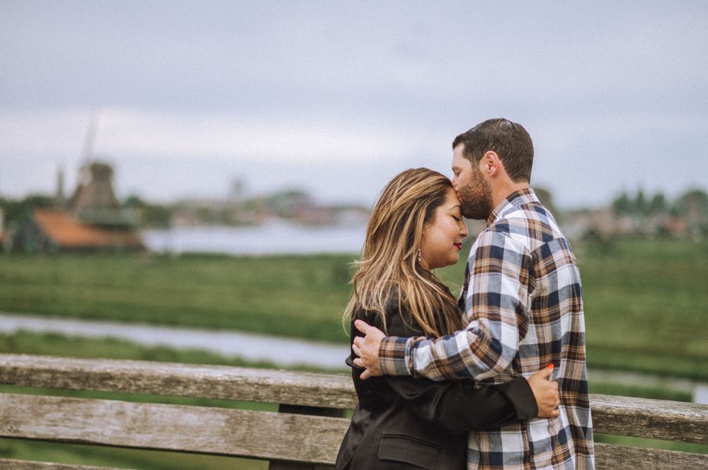 Couple sharing tender moment on rustic wooden fence with countryside backdrop.
