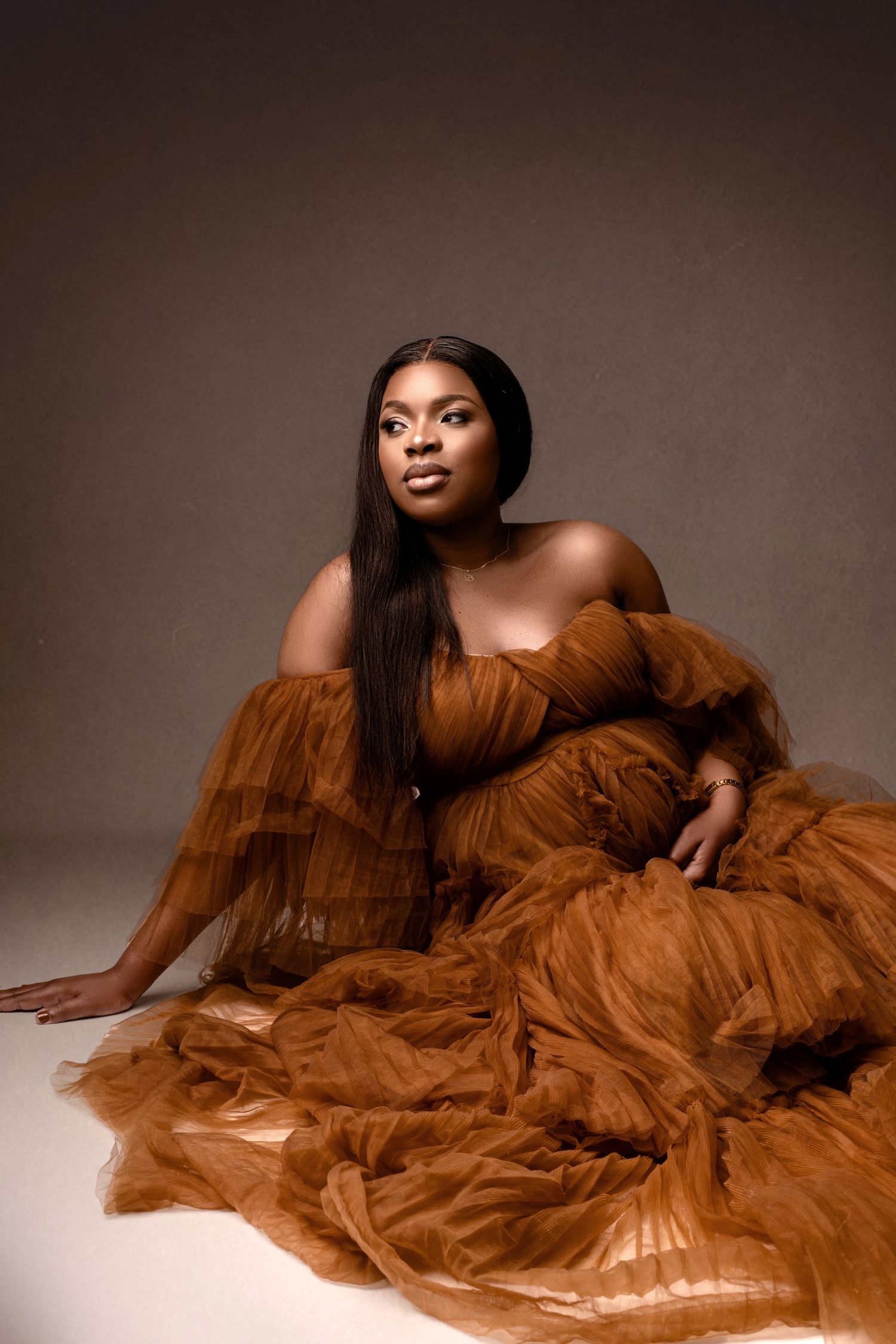 A dramatic portrait featuring a flowing rust-colored tulle gown against a brown backdrop.