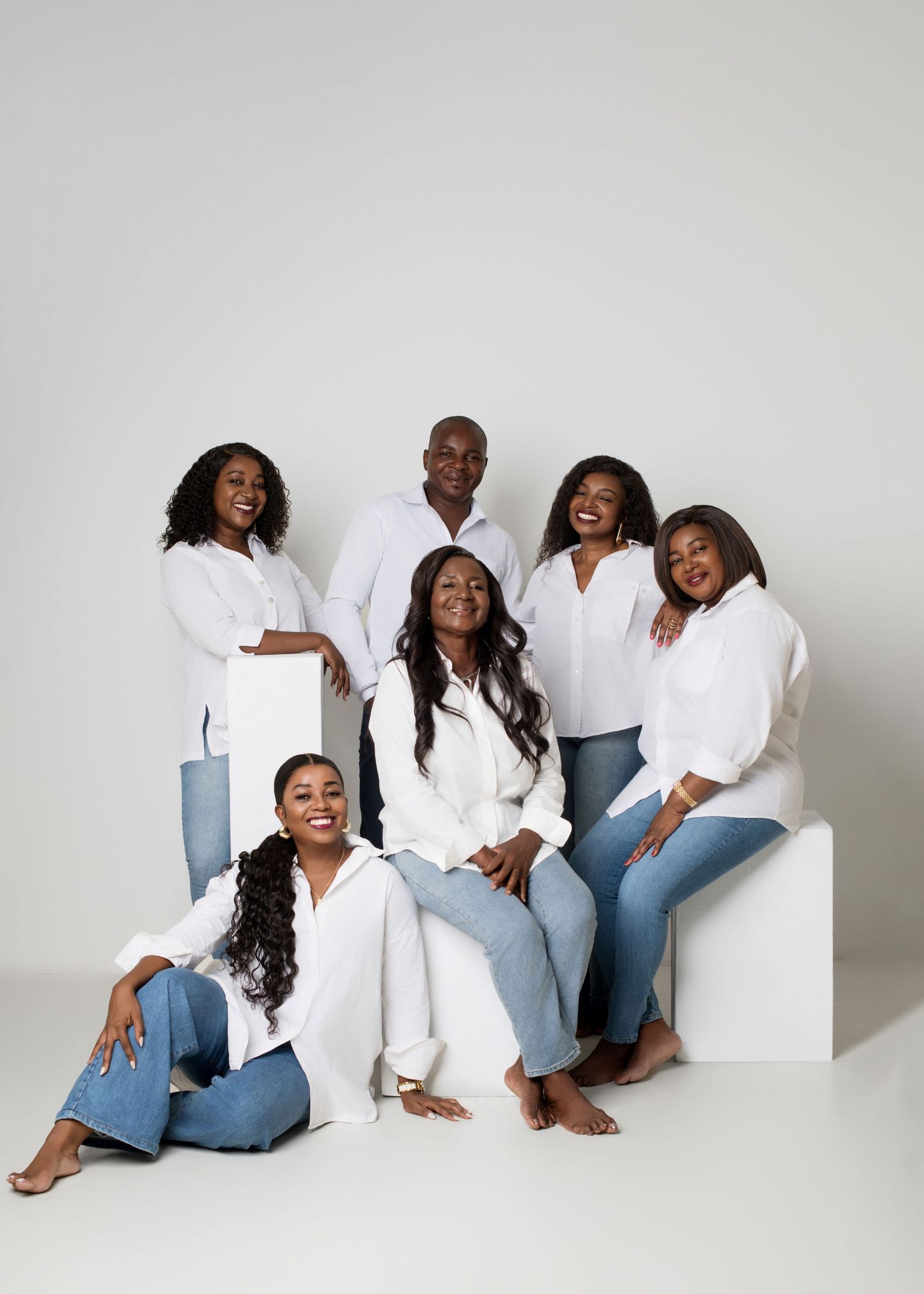 A group of people wearing coordinated white tops and blue jeans pose together against a light gray background.