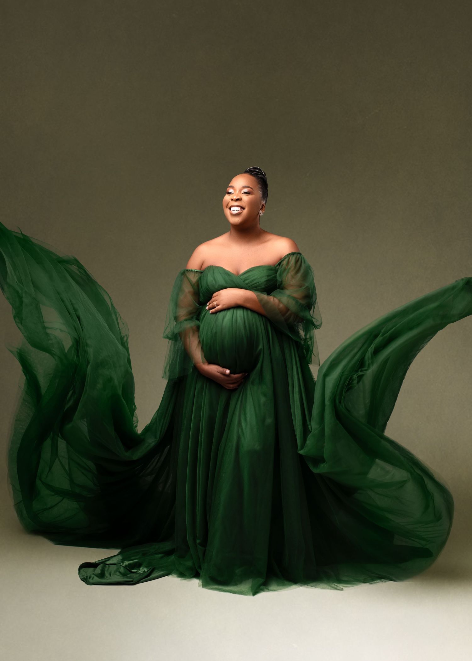 A maternity portrait in an emerald green flowing gown with dramatic fabric movement.
