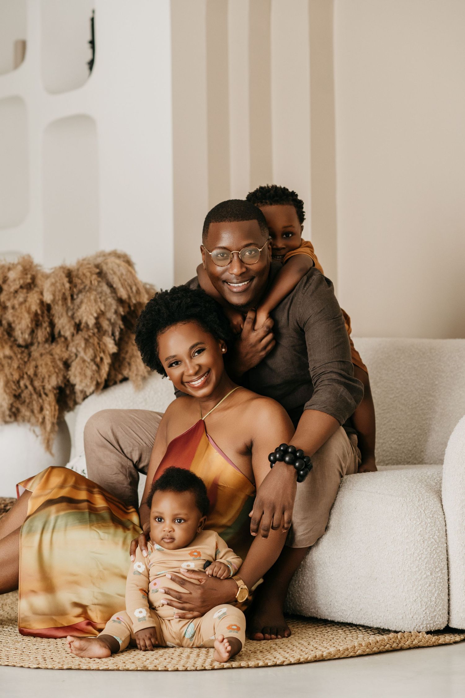 A family relaxes together on a white couch with pampas grass decor in the background.