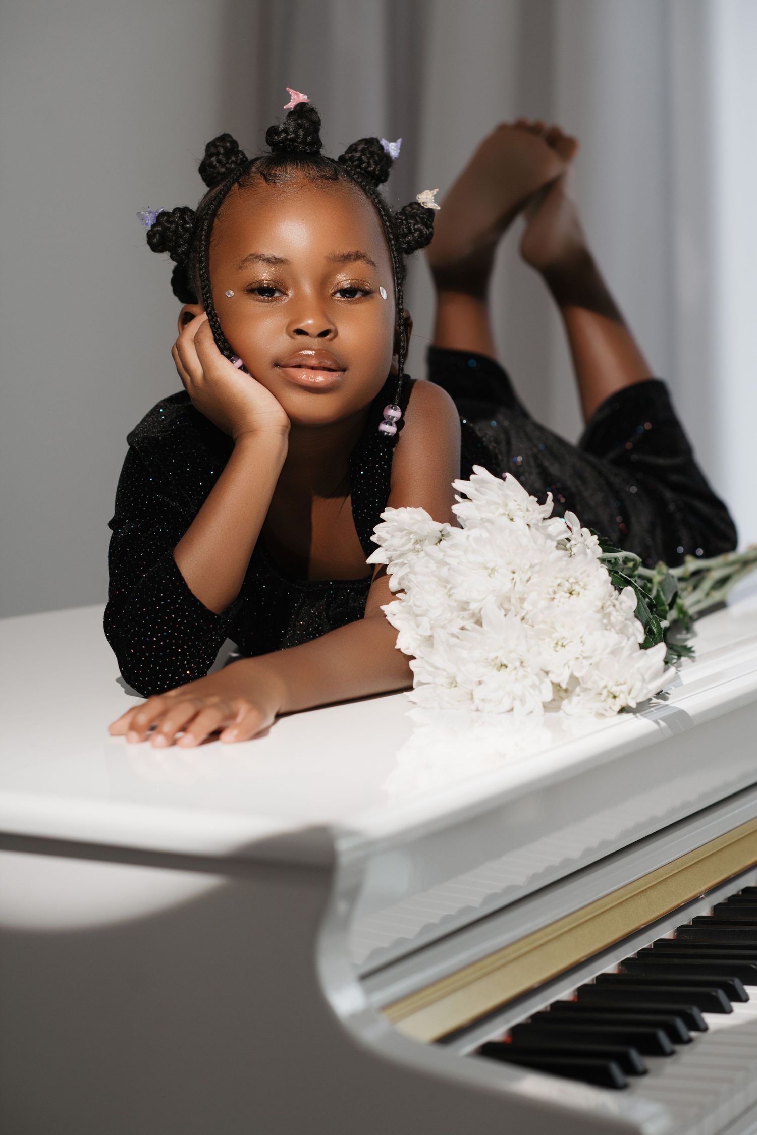 Young girl with bantu knots poses on white piano with white flowers.