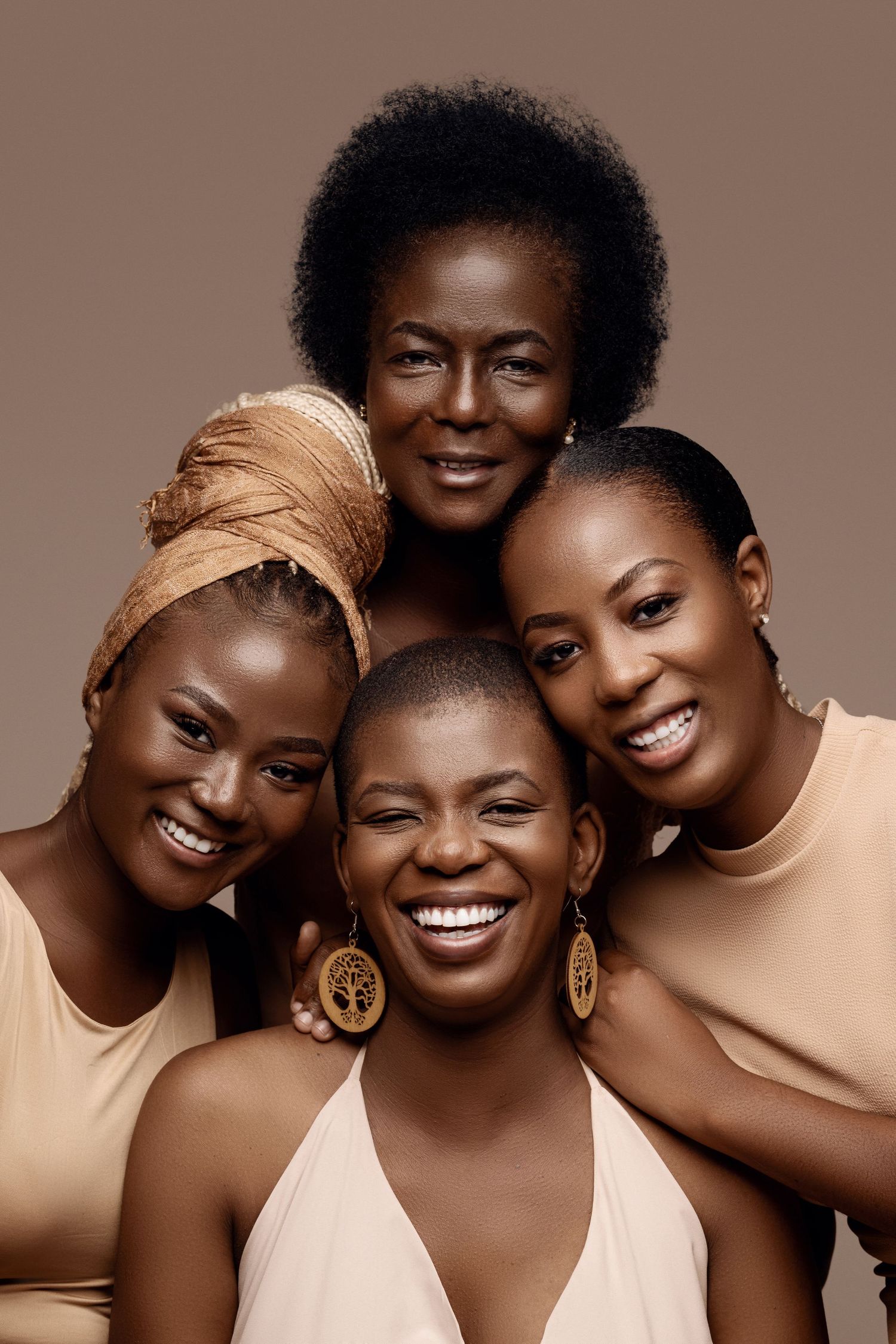 Artistic portrait of four women in neutral tones against brown background.