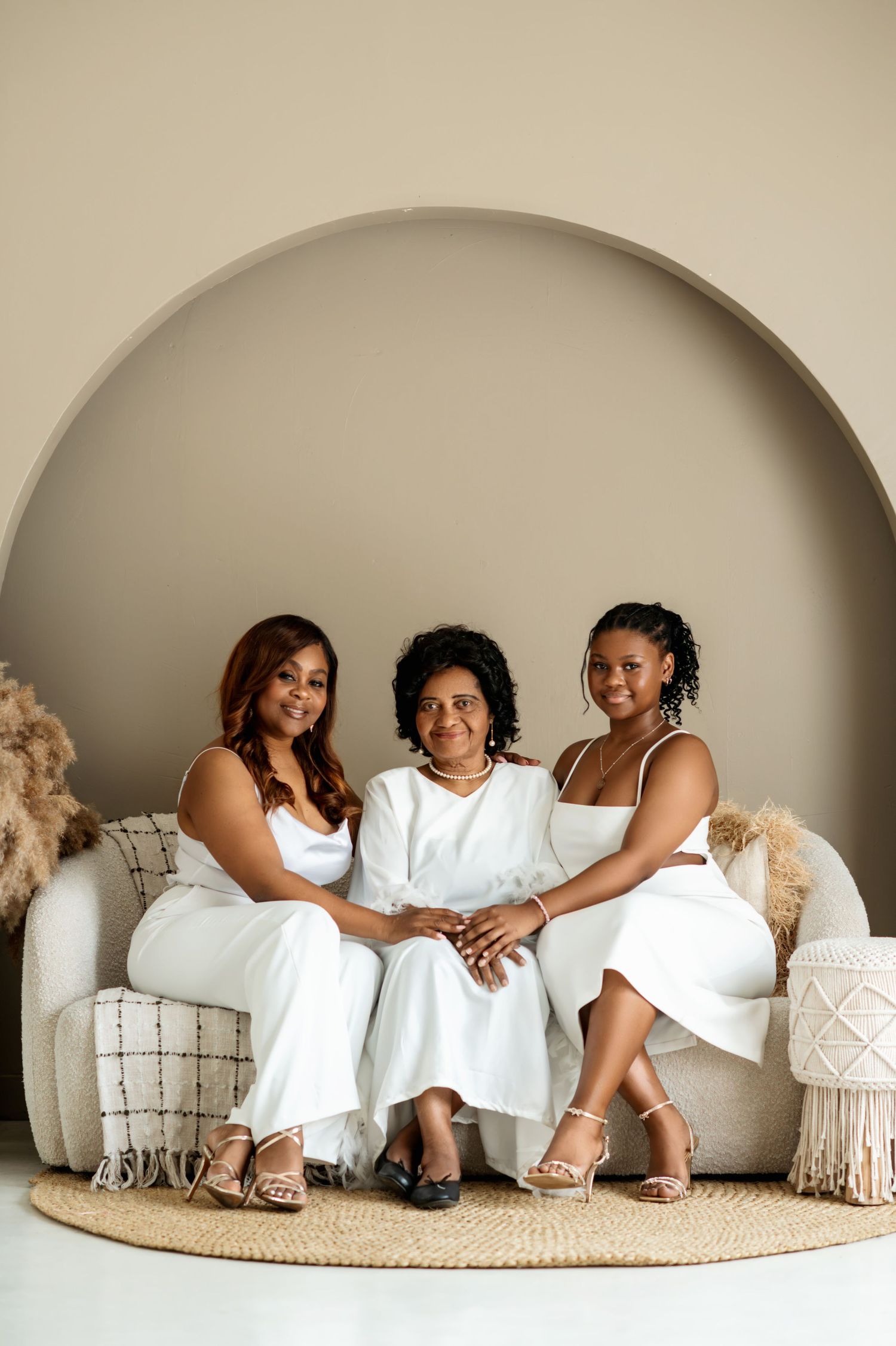 Three generations pose together on a white couch in matching white outfits.