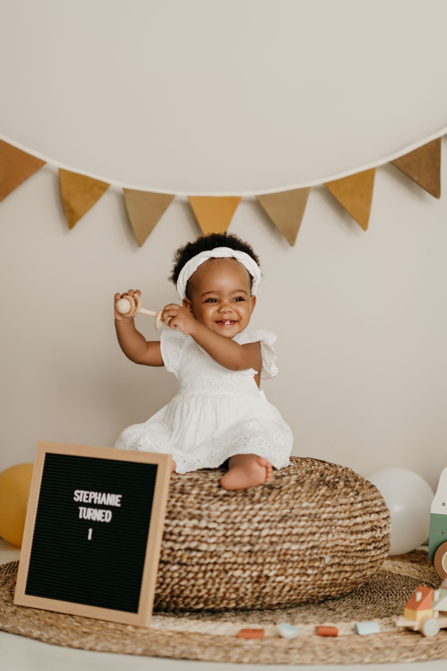 Decorative mustard and brown triangle banner hangs above pouf with letterboard and baby accessories in neutral nursery setting.
