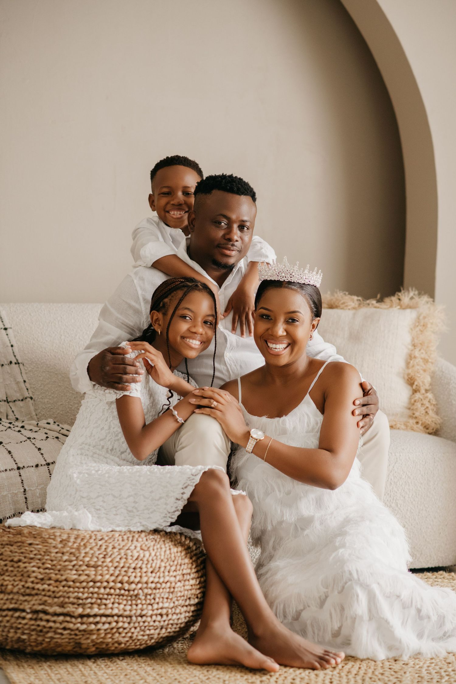 A joyful family portrait of four people sitting on a cream-colored couch.