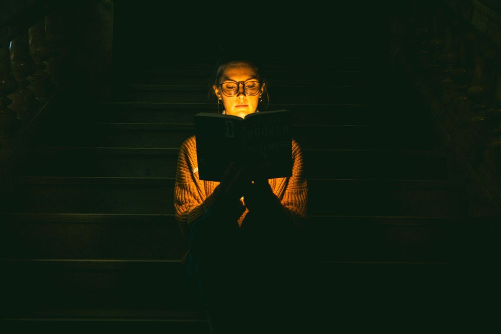 Dark moody portrait with orange light illuminating a figure holding a book in a dimly lit stairwell.