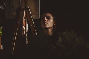 An artist works in low light conditions near an easel creating a mysterious atmosphere.