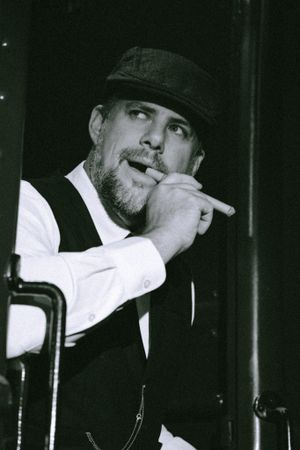 A noir-style portrait of someone in a fedora and vest smoking in dramatic lighting.