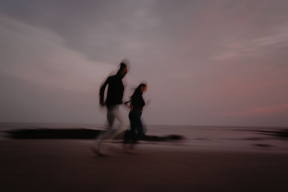 Blurry motion shot of two people running on a beach at dusk with a pink and purple sky.