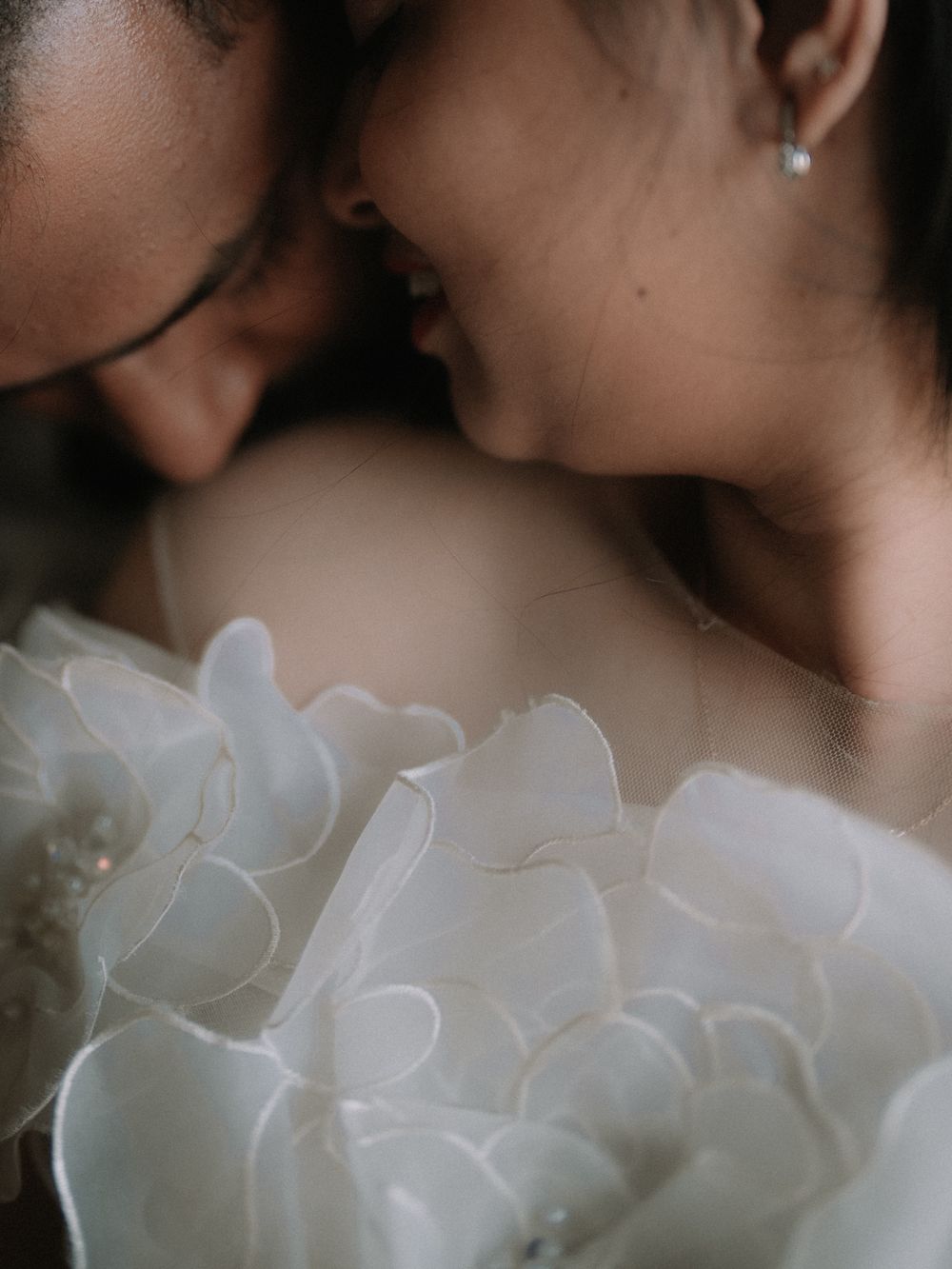 Close-up of a couple in an intimate moment, bride wearing a stunning white floral petal wedding gown.