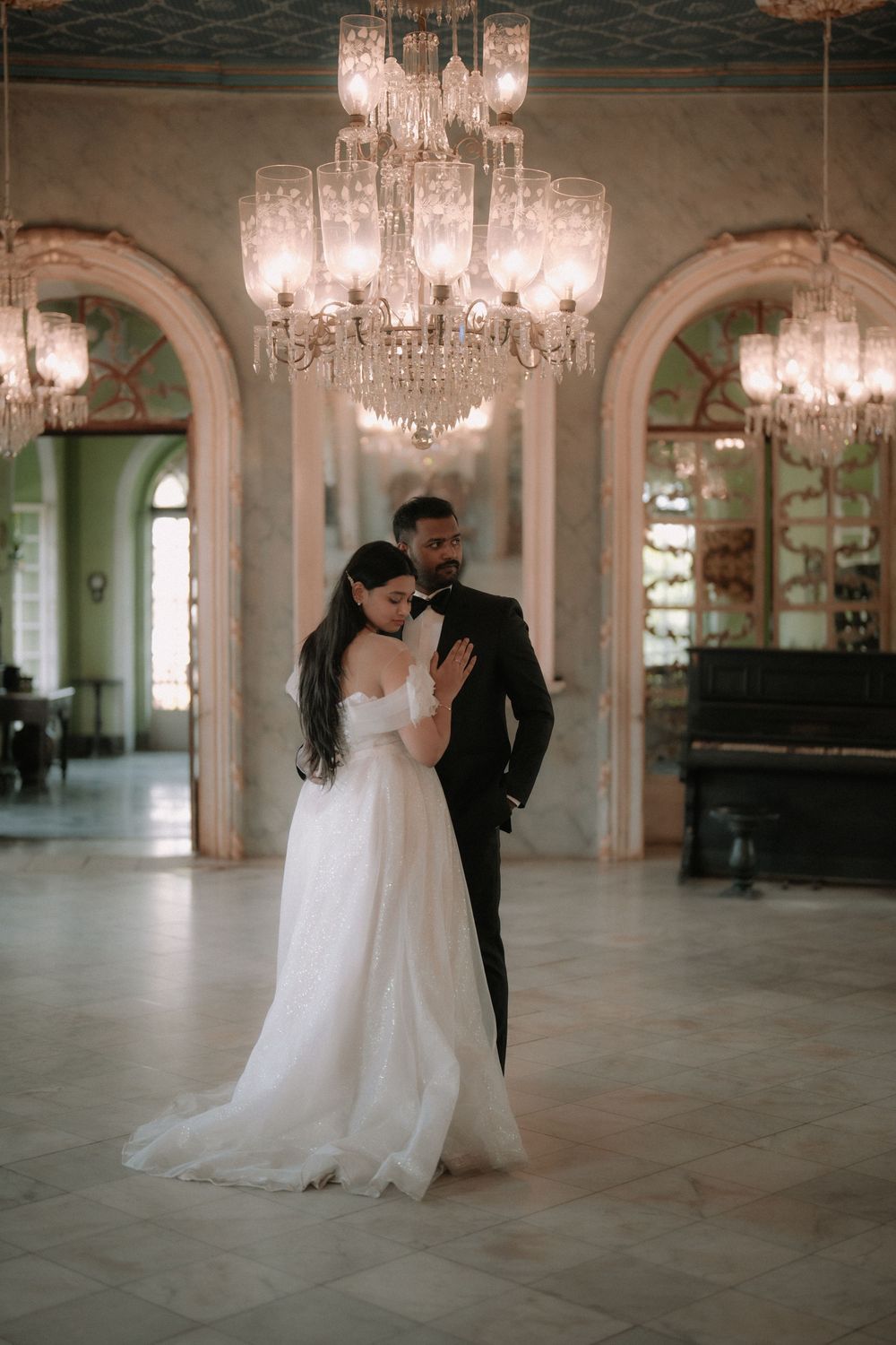 Bride and groom share an intimate moment under crystal chandeliers in an elegant marble ballroom.