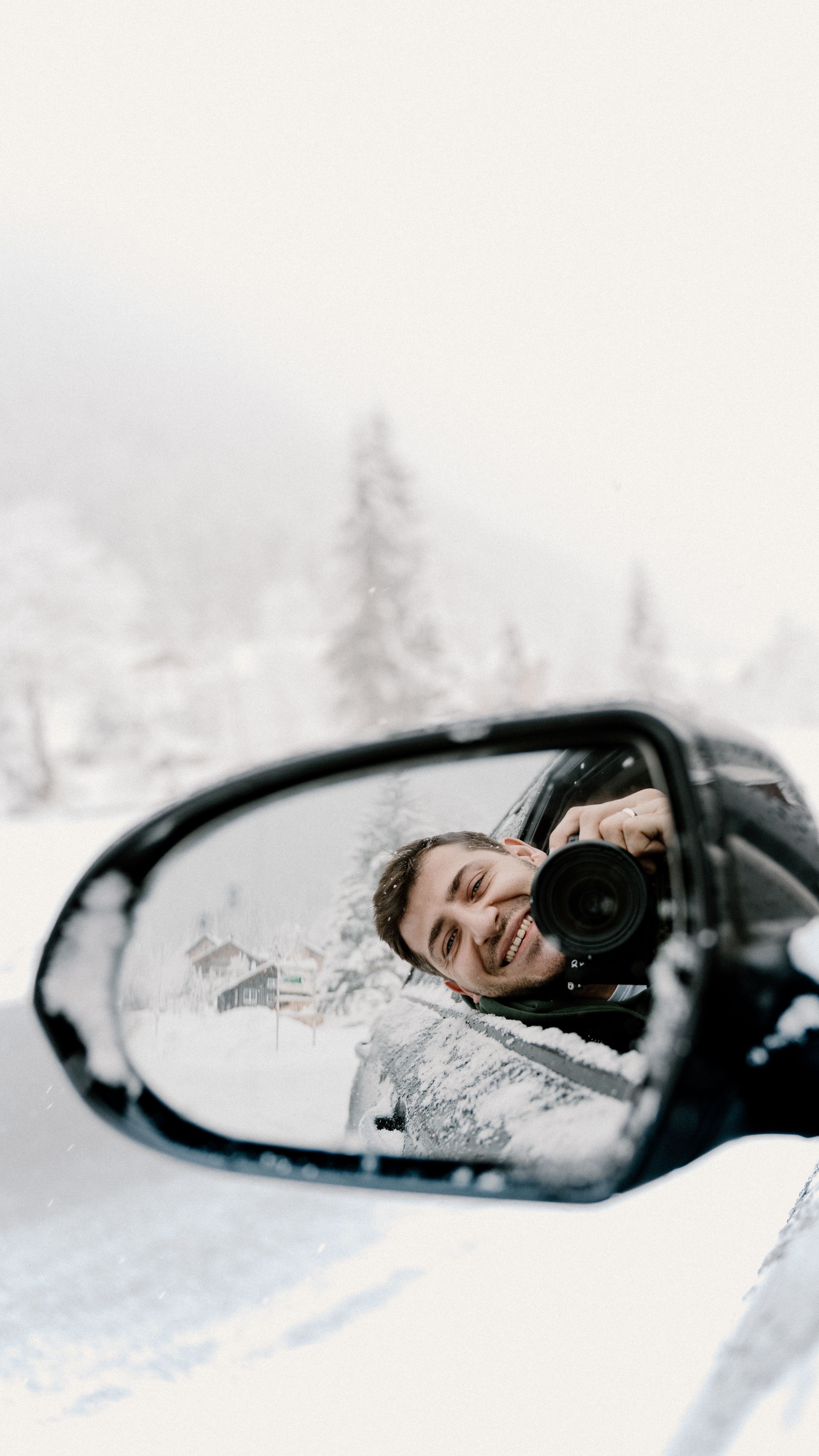 Winter reflection in car side mirror shows snowy landscape in background.