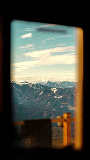 Snow-capped mountain peaks viewed through a window frame against a bright blue sky.