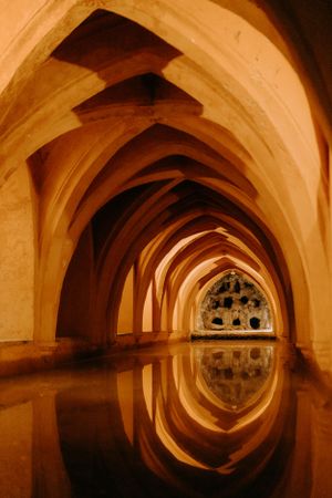 Gothic arches create a mirror-like reflection in the flooded undercroft of a historic building.