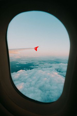 View of clouds and airplane wing through passenger window during sunset flight.