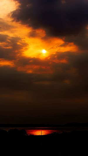 Dramatic orange sunset over water with dark storm clouds and reflections.