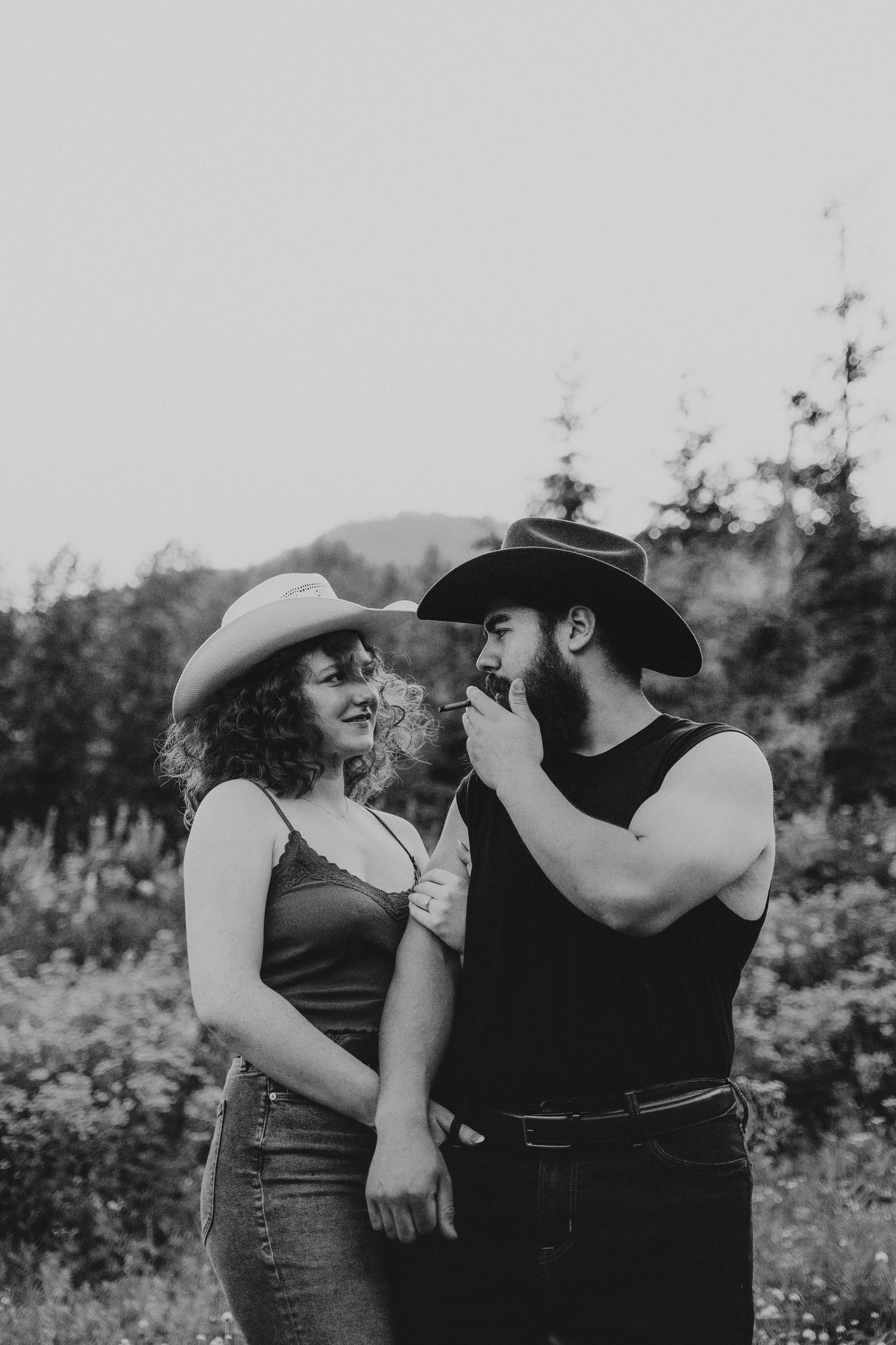 A couple shares an intimate moment in a rustic outdoor setting wearing western-style attire.