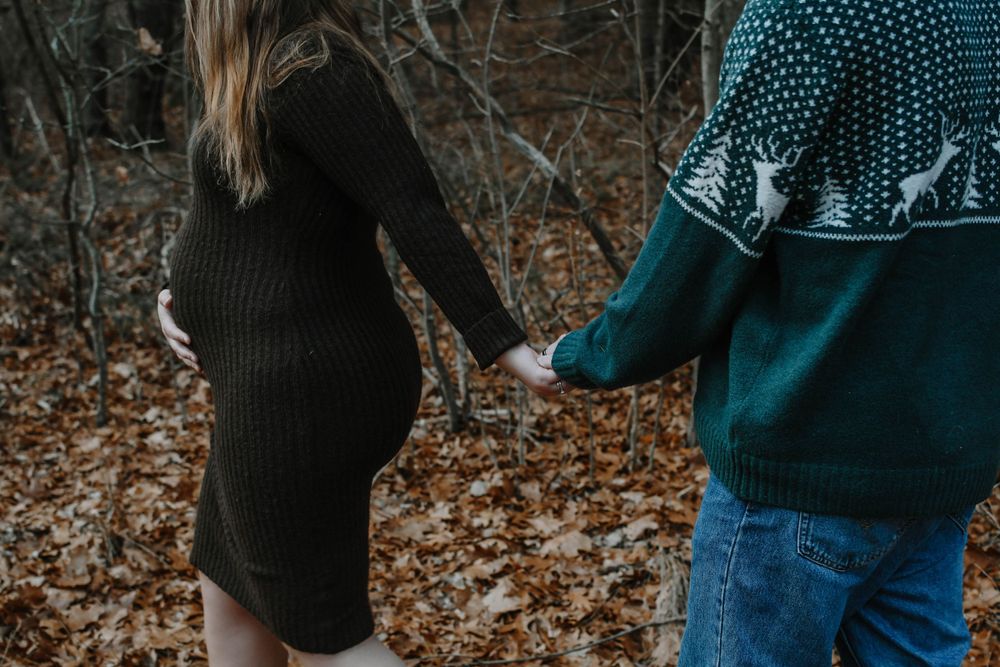 A person in teal sweater holds hands with someone wearing black dress while walking through autumn leaves.