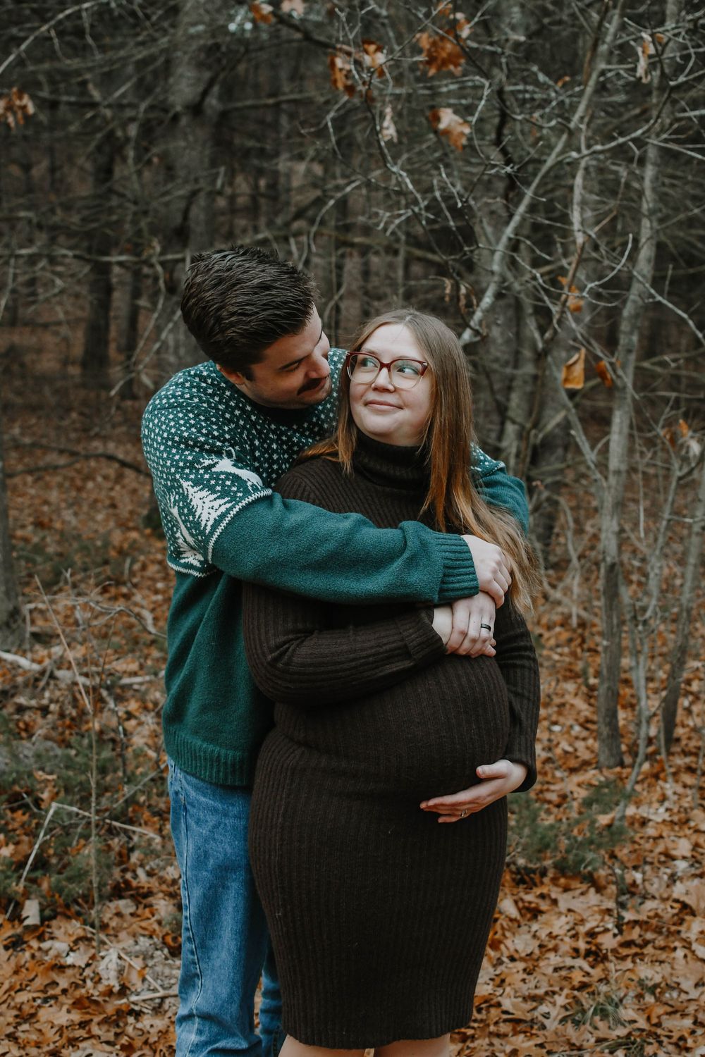 Couple embraces in autumn forest with falling leaves as they share a tender moment outdoors.