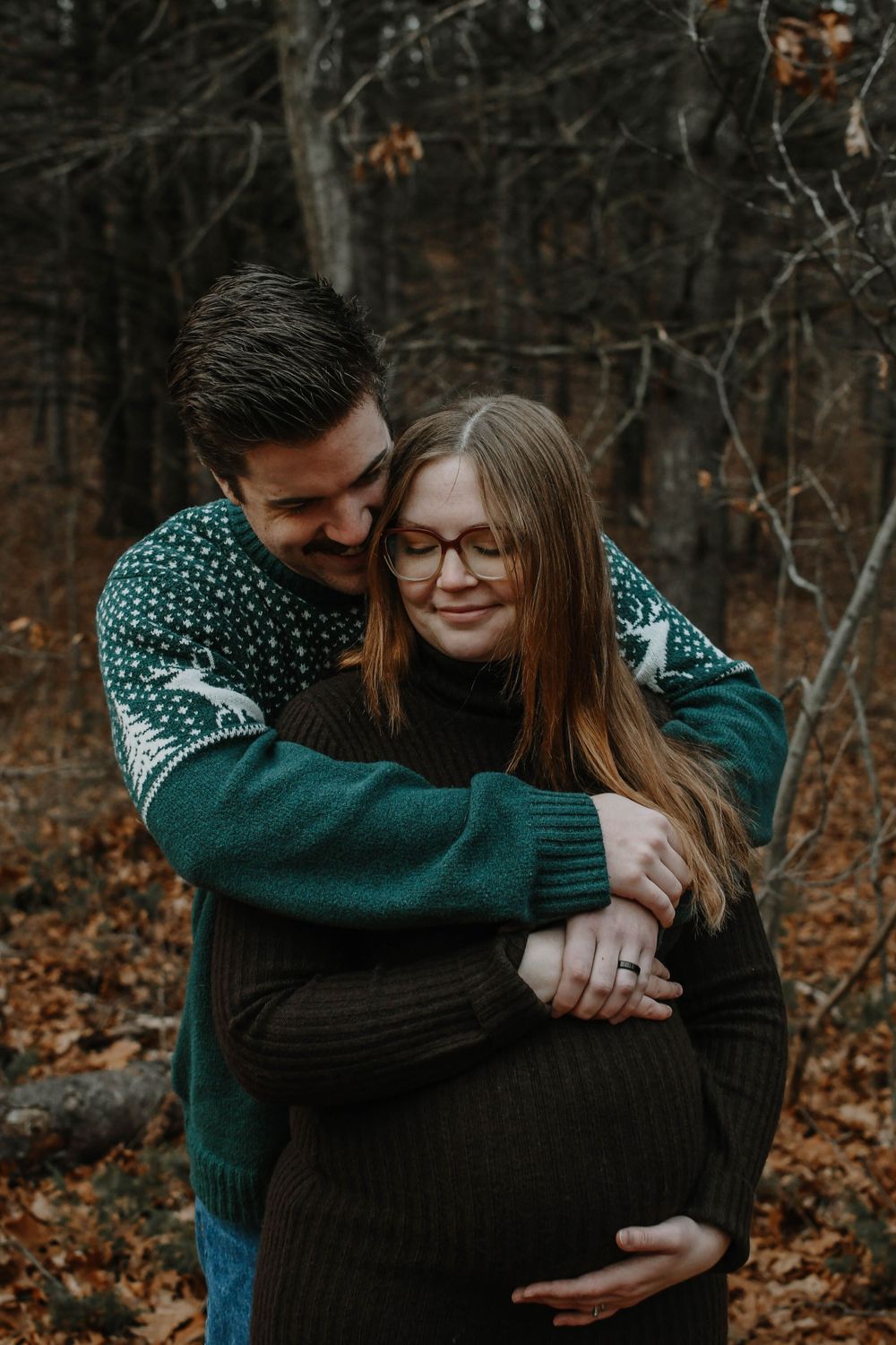A loving couple in matching green sweaters share a tender embrace in an autumn forest setting.