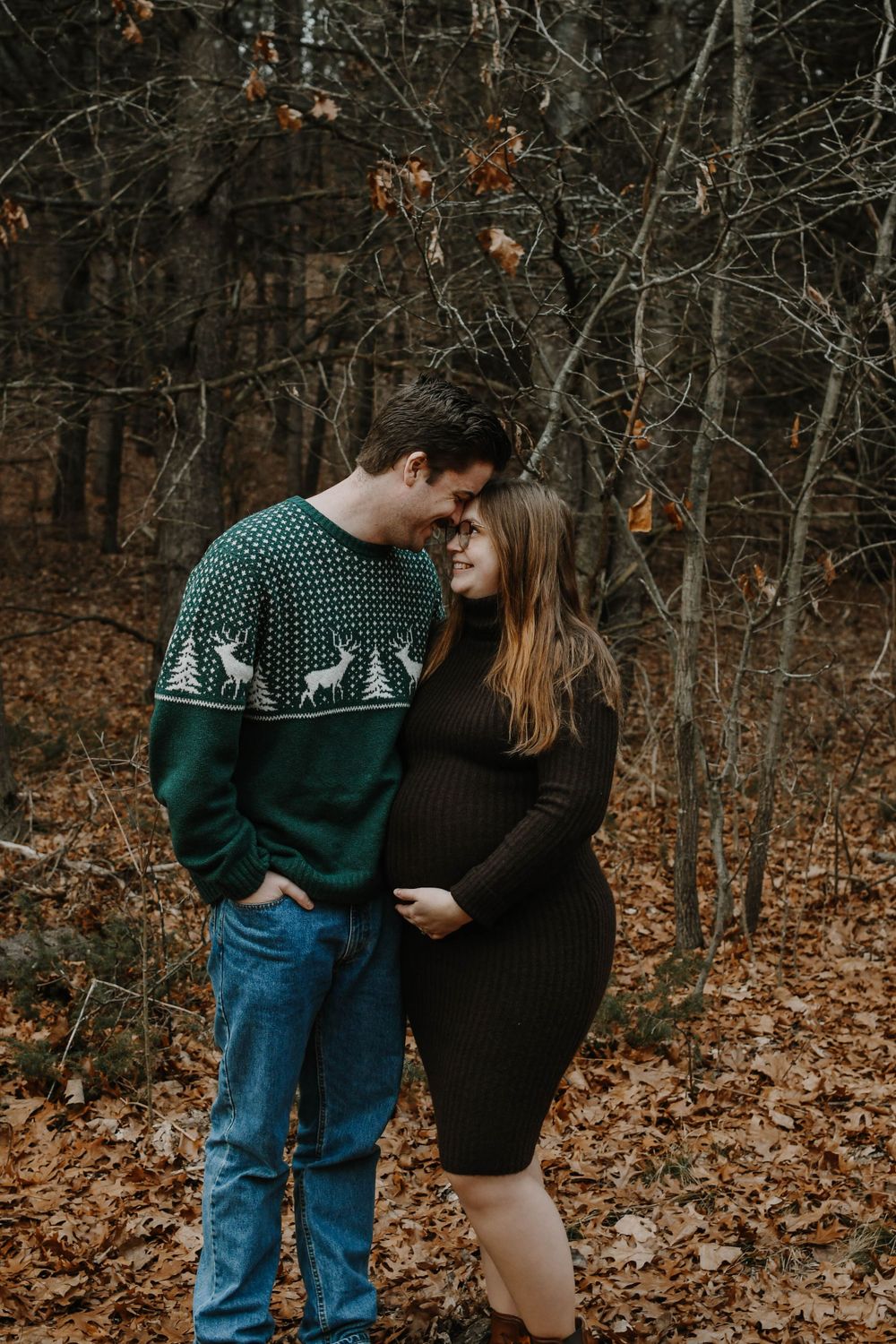 A couple shares an intimate moment in a fall forest setting, with one wearing a festive green patterned sweater.