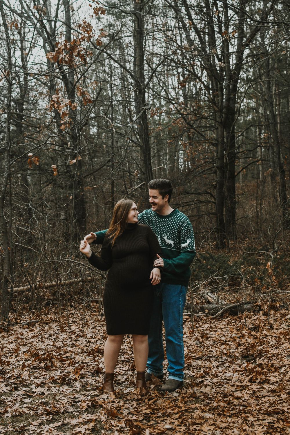 A couple standing on autumn leaves in the woods sharing a romantic moment while wearing cozy winter attire.
