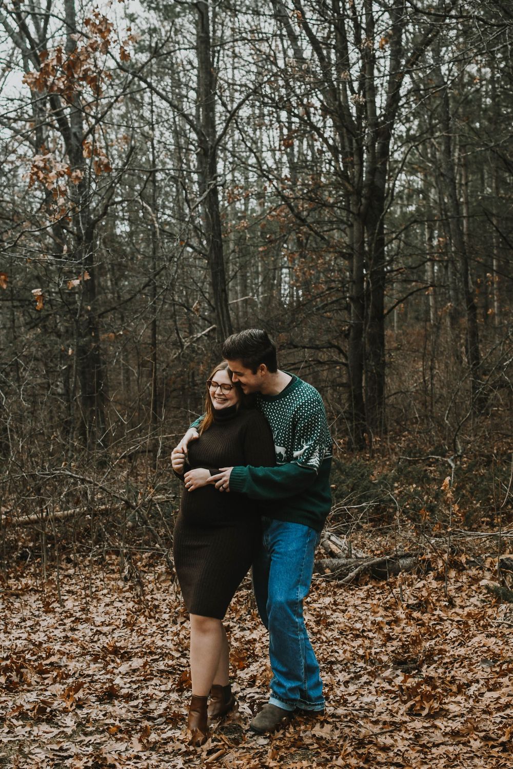 A tender embrace between a couple on fallen autumn leaves in the woods as they share a quiet moment together.