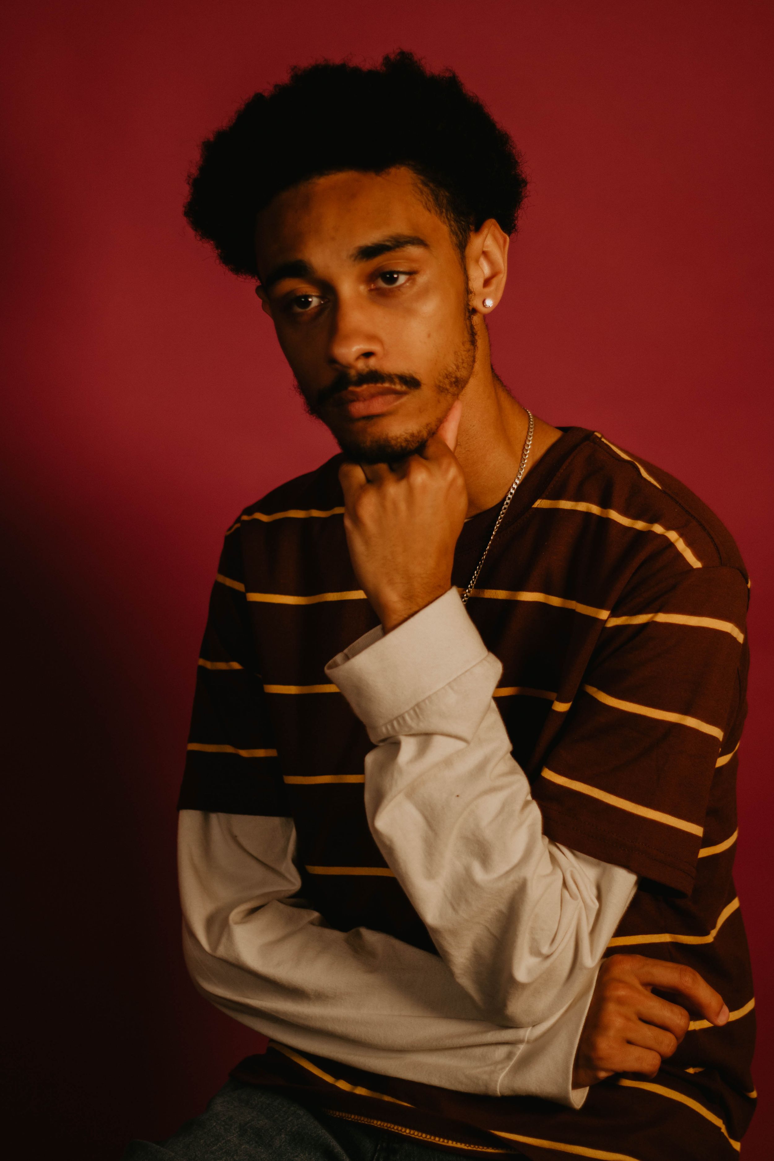 Portrait of model in brown striped sweater against red backdrop with moody lighting.