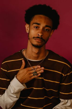 Portrait shot of model in layered brown striped sweater with necklace against red backdrop.