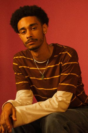 Model poses in casual brown and tan striped layered sweater against red background.