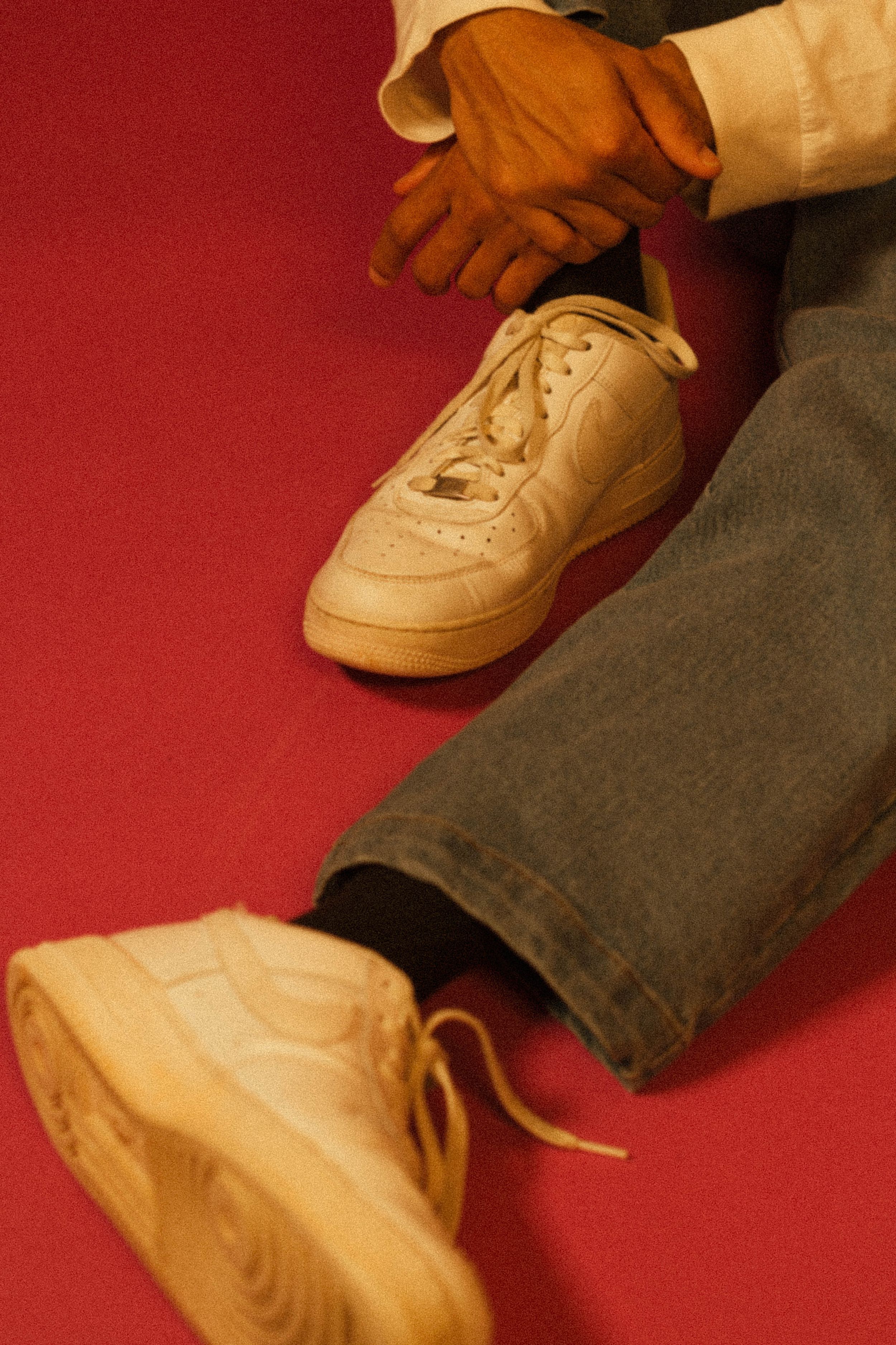Close-up of tan sneakers and jeans against red background.